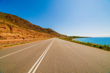 asphalt interstate road between yellow sedimentary rock mountain and large lake at sunny summer...