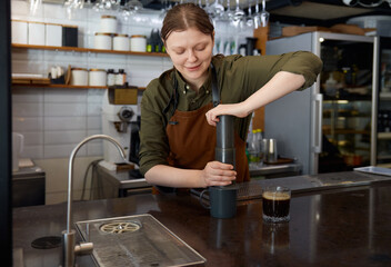 Woman barista using aeropress coffeemker for coffee preparation
