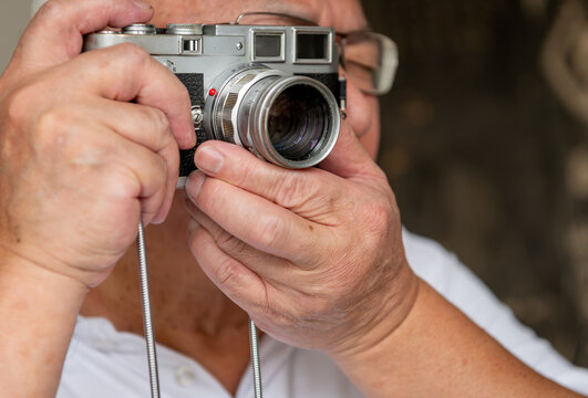 A senior man using a classic vintage camera to take photos. - Powered by Adobe