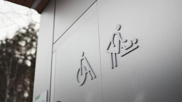 Restroom for guests with disability and mother with baby in winter urban park. Information symbols on door of street WC. City hygiene utility