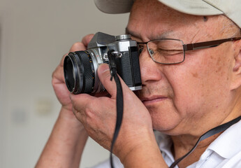 A senior man using a vintage SLR photography film camera to take pictures.