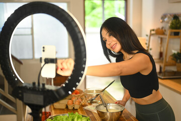 Attractive young female blogger recording video vlog about preparing a nutritious recipe in kitchen