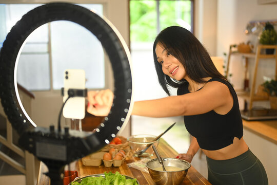Attractive young female blogger recording video vlog about preparing a nutritious recipe in kitchen