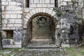 Fototapeta premium Archway leading into Strada del Soccorso in Brescia castle with detailed stone textures. The composition highlights the depth of the staircase and arch