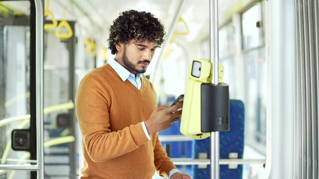 Man using smartphone for fare payment on public transport, standing in modern tram Male paying public city or bus with mobile phone app. validating ticket ride inside trolleybus use application