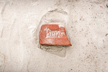 Red brick with Cyrillic text partially buried in sand, emphasizing pollution problems on Russian...
