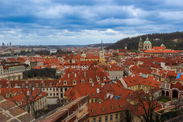 Obraz premium A panoramic view of the historic Prague cityscape with red roofs and architectural landmarks under a cloudy sky, ideal for travel and tourism