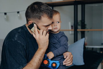 Fatherhood concept, boy son hugs father tightly and cries. Young dad calls his wife for advice on...