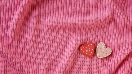 A pair of intricately decorated heart-shaped cookies rests atop a textured pink surface