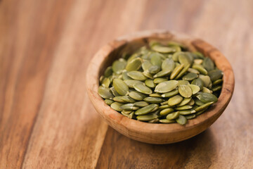 green pumkin seeds in bowl on wooden table