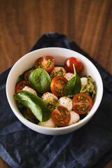 Caprese salad variation with pesto and spinach in white bowl on walnut table