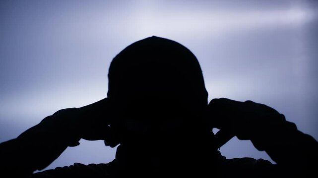 robbery and theft concept, adult man in black balaclava putting hood on head in backlight