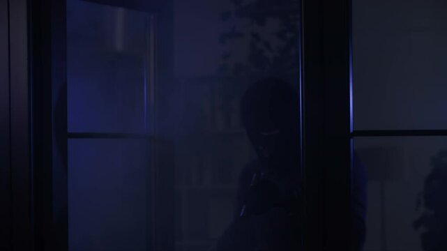 burglary, adult male in black clothes and balaclava with flashlight in hand enters room looks around at night