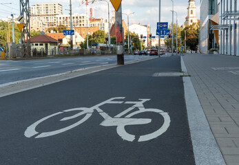 Empty bicycle lane with a white bike symbol in an urban setting, leading toward a busy city street lined with modern buildings. Comfortable urban infrastructure for bicyclists. High quality photo