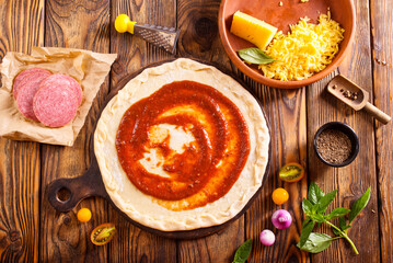 Raw pizza dough with tomato sauce and basil leaves.