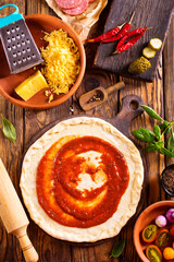 Raw pizza dough with tomato sauce and basil leaves.