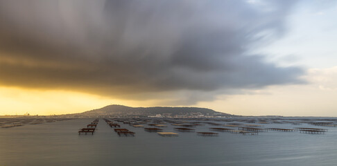 Obraz premium Mont Saint Clair and the Thau lagoon, with its oyster tables, under a stormy sky, in Hérault, Occitanie, France