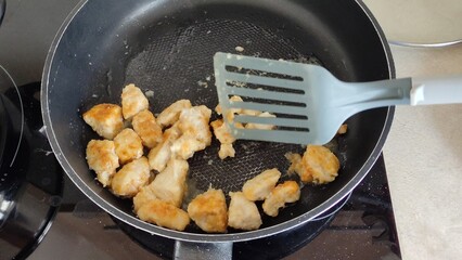 Man stirs chicken breast pieces fried in a frying pan with a spatula