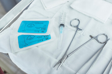 A sterile medical setup featuring surgical tools, sutures, and a syringe on a white cloth. Ideal...