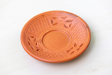 A beautifully crafted round clay plate on a light wooden surface. Empty earthenware plate.