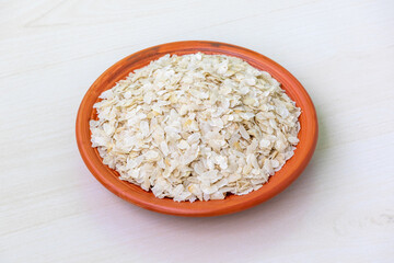 Raw flattened rice or chira on a clay plate on a light wooden surface. It is also known as poha, pohe, aval, pauwa, sira, chivda, or avalakki.