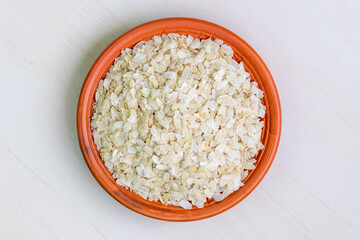 Raw flattened rice or chira on a clay plate on a light wooden surface. It is also known as poha, pohe, aval, pauwa, sira, chivda, or avalakki. Top view.