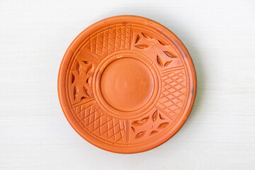 A beautifully crafted round clay plate on a light wooden surface. Top view of an empty earthenware plate.