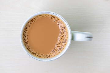 A cup of milk tea or dudh cha in a ceramic cup on light wooden surface. Top view.