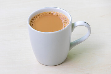 A cup of hot milk tea or dudh cha in a white ceramic cup on light wooden surface.