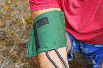 green medical rubber cuff with black hoses applied to patient's arm in red t-shirt to measure blood...