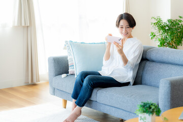 部屋でスマホを操作するミドル女性