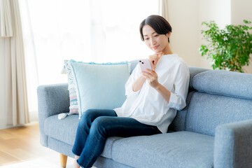 部屋でスマホを操作するミドル女性