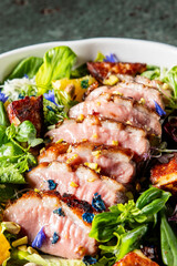 A gourmet dish featuring sliced grilled meat on a bed of fresh greens, garnished with vibrant edible flowers. The colorful presentation highlights the contrast between the cooked meat and fresh salad