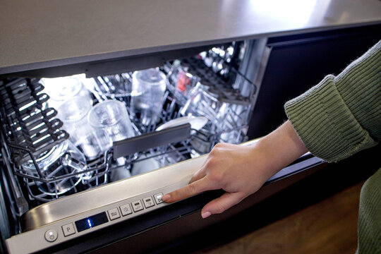 Woman's hand turns on the dishwasher to wash the dishes. Built-in appliances in the kitchen.