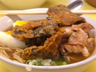 A delicious bowl of ramen served with crispy fried fish, tender slices of meat, soft-boiled eggs with vibrant orange yolks, fresh vegetables, and noodles in a savory broth