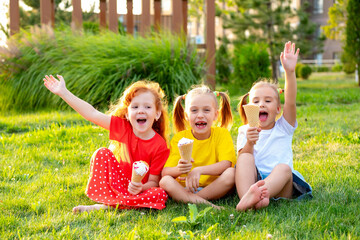 happy children eating ice cream in the summer on the green lawn in the park, a bright summer photo of children's holidays, three baby girls laughing and having fun in the summer