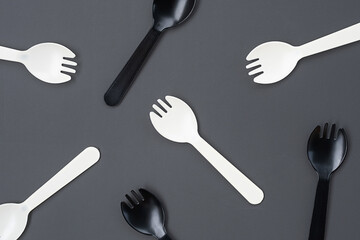 Black and white plastic forks on gray background. Disposable cutlery and minimalism concepts.