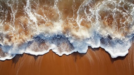 Aerial view of ocean waves crashing onto a sandy beach, creating white foam patterns