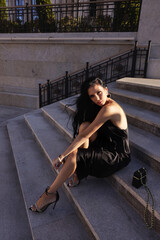 beautiful woman with dark hair in elegant black dress and accessories posing in beautiful villa