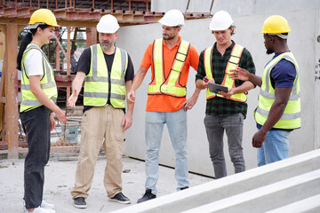 Male and female engineers stand in a planning meeting at a construction site.