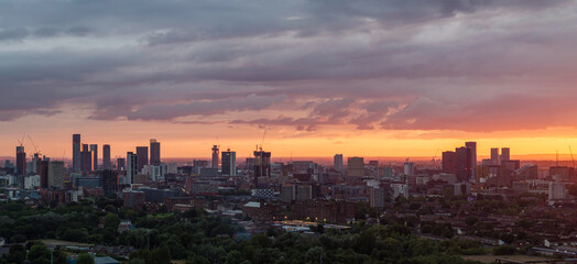 A panoramic view of Manchester city skyline at sunset, with dramatic clouds and a warm color palette.