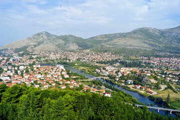 Fototapeta premium Panoramic view of Trebinje with Trebišnjica river and Arslanagica bridge. Beautiful landscape from Bosnia and Herzegovina: aerial view of red roofed houses, mountains, greenery and river.