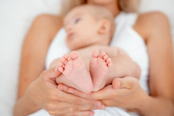 mom's hands hold the legs of a newborn baby, legs in focus, pink baby heels