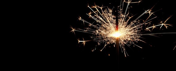 Fototapeta premium Close-up of a glowing sparkler firework against a black background with copy space. New year party concept. 