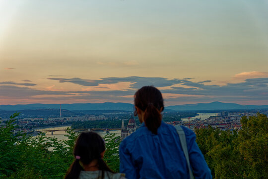 A woman and a child stand together looking over the beautiful Budapest cityscape during a colorful sunset. Such peaceful travel moments capture the deep bond of family and the joy of shared discovery.