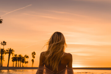 Fototapeta premium young blonde woman bathes on the beach in the warm sea with palm trees at sunset