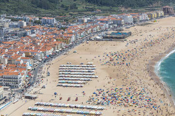 Nazaré sand beach and boulevard on a summer day with a beach full of people at Nazare Portugal. © PixelBiss