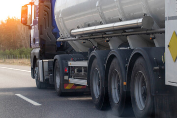 A tanker semi-trailer truck transports a dangerous cargo of gasoline, diesel fuel and petroleum products on the road against the backdrop of the sun. Cargo hazard class. Copy space for text