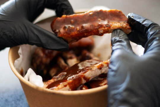 Grill restaurant kitchen food delivery. Man in black gloves holding grilled pork ribs with bbq sauce from the cartoon plate.