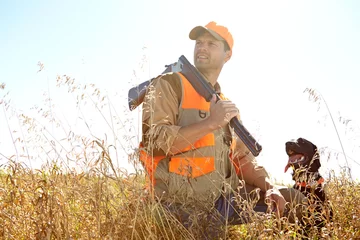 Fotobehang Man, dog and outdoor for hunting gear, shotgun and search for prey together in nature. Mature person, pet animal and hunter support in field to guide in woods, confused and thinking on wildlife © ReeseBuyout3/peopleimages.com